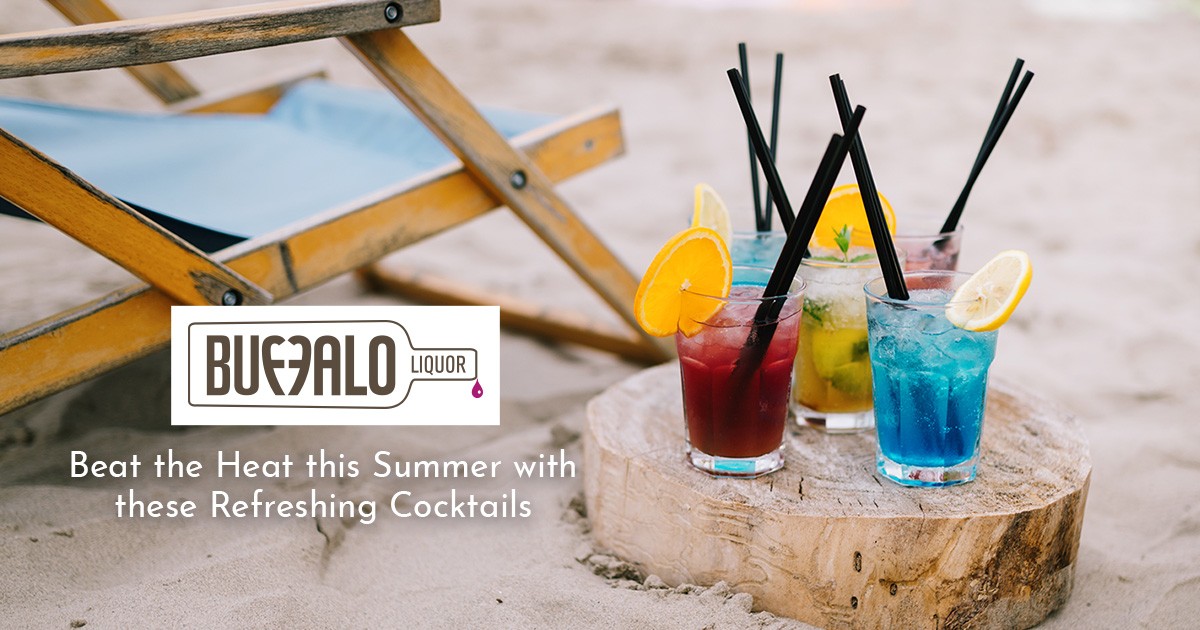 Four colorful cocktails with fruit garnishes on a beach, next to a wooden chair and log table.
