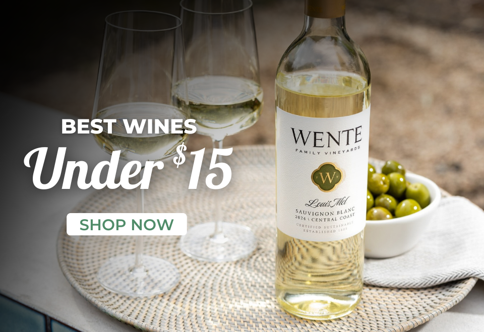 A bottle of Wente white wine, two glasses, and a bowl of green olives on a table.