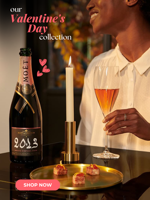 A woman holds a champagne glass beside a bottle, candle, and treats for Valentines Day.