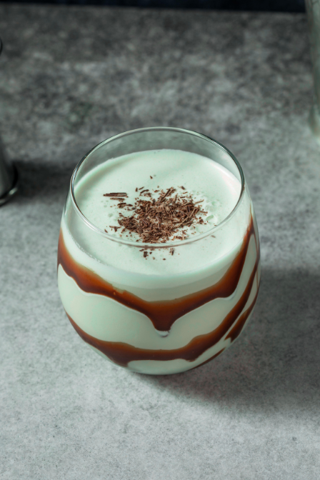 A creamy green cocktail in a glass with chocolate swirls and chocolate shavings on top.